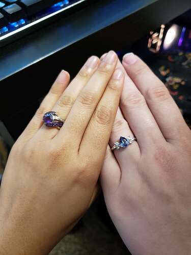 A photo of the wedding rings. One is a thicker band with an amethyst. The other is a thinner band with a sapphire and decorative diamond leaves.