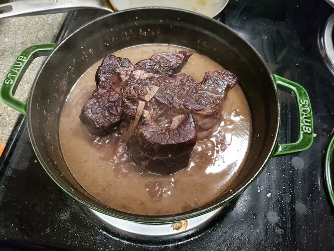 A cast iron pot with braising beef. The beef is shaped like a wonky fleur-de-lis.