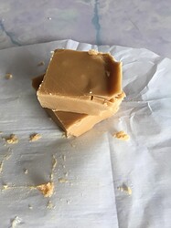 Two pieces of fudge stacked on top of each other, atop the sheet of flattened parchment paper it set in