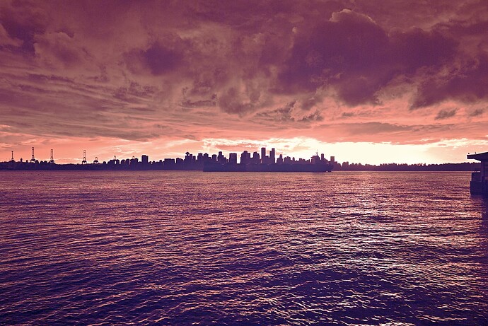 A downtown skyline under a turbulent, cloudy sky, with the sun setting off in the background. Everything is in purples, reds, and oranges.