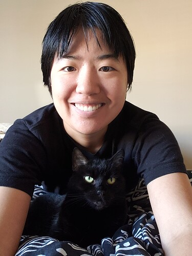 Chinese trans man posing with a black cat. The cat is loafing and looking directly at the camera.