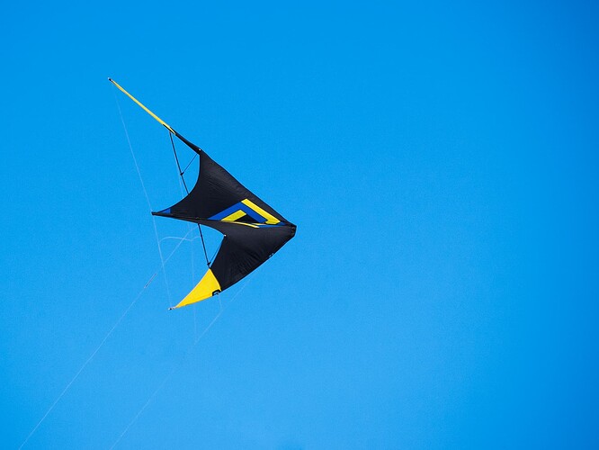 A black and yellow kite flying against a cloudless blue sky.